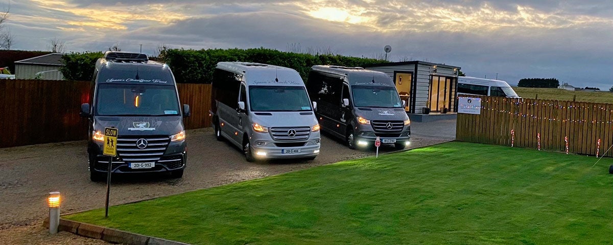 Three Mercedes class mini buses parked together at dusk with their lights on