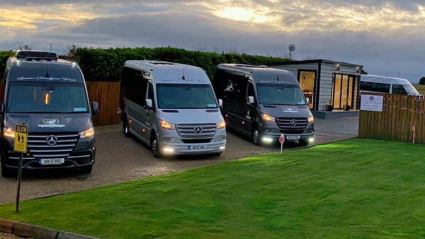 Three Mercedes class mini buses parked together at dusk with their lights on