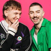 2 laughing men against bright pink background.