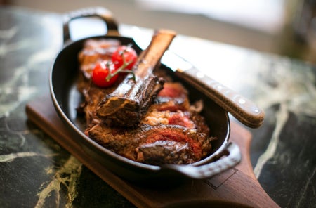 A small pan with a steak garnished with some herbs and tomatoes