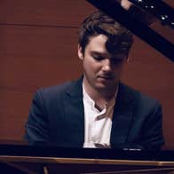 A man looking down at keyboard, seated at a grand piano