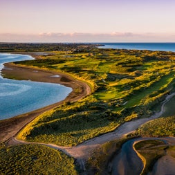 Aerial view of golf course surrounded on either side by the sea and a beach on the left