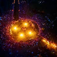 Viewed from above at night, a large crowd gathered around a large circle containing 4 fires.