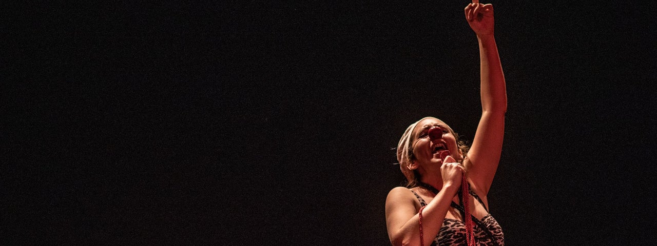 Dark stage with person holding a mic with the other hand up in the air.