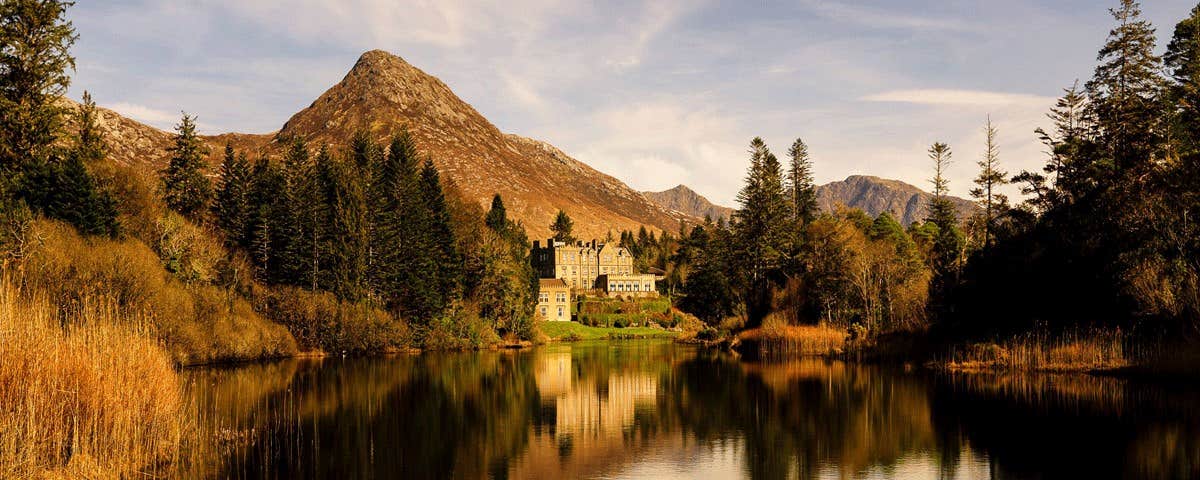 An autumnal morning view of Ballynahinch Castle from across the lake with trees and hills in the background