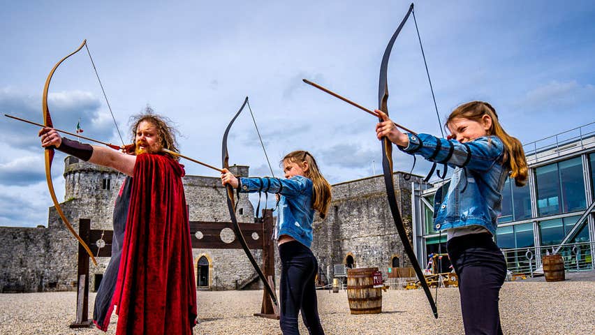 The castles resident archer with two girls all holding their bow and arrows in the courtyard