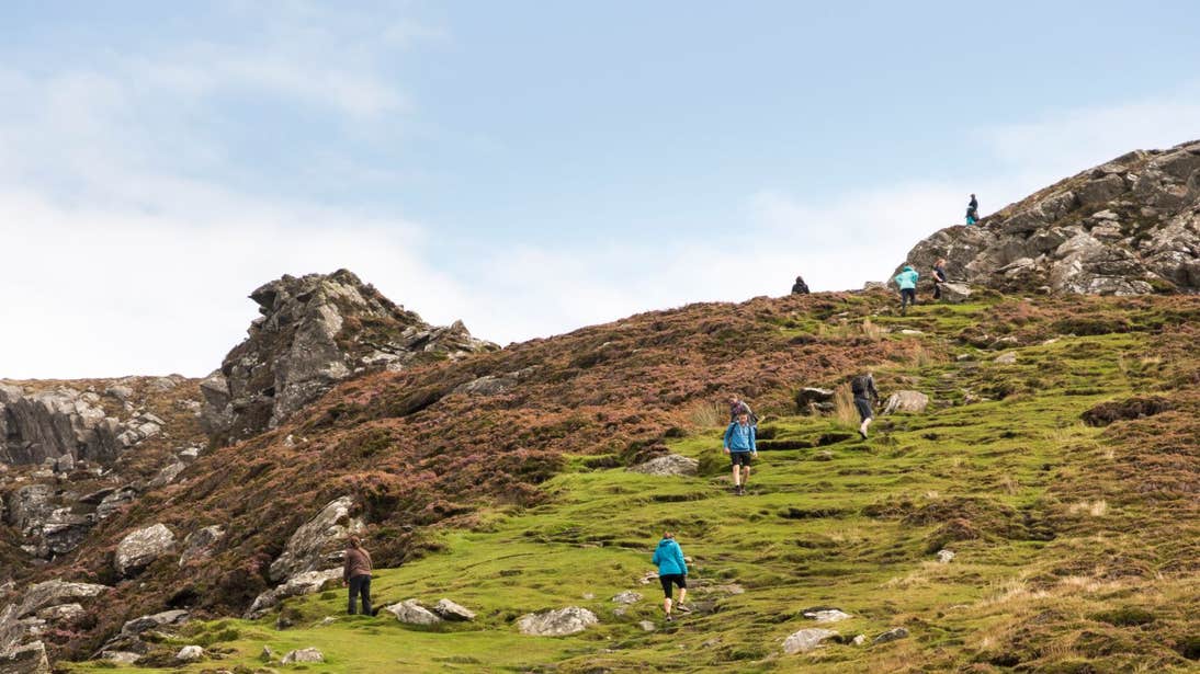 A group of people walking up a green hill at Sliabh League, Donegal