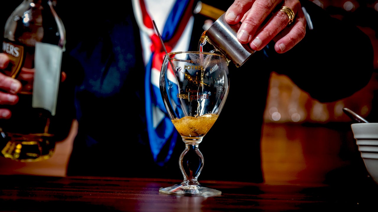 The Irish Coffee Experience, view of a person pouring from a small, silver jug into a glass with a stem.