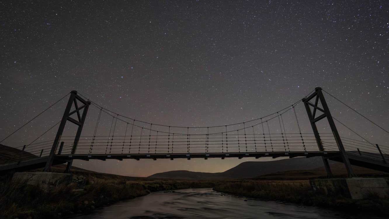 A darkened sky with stars behind a raised footbridge