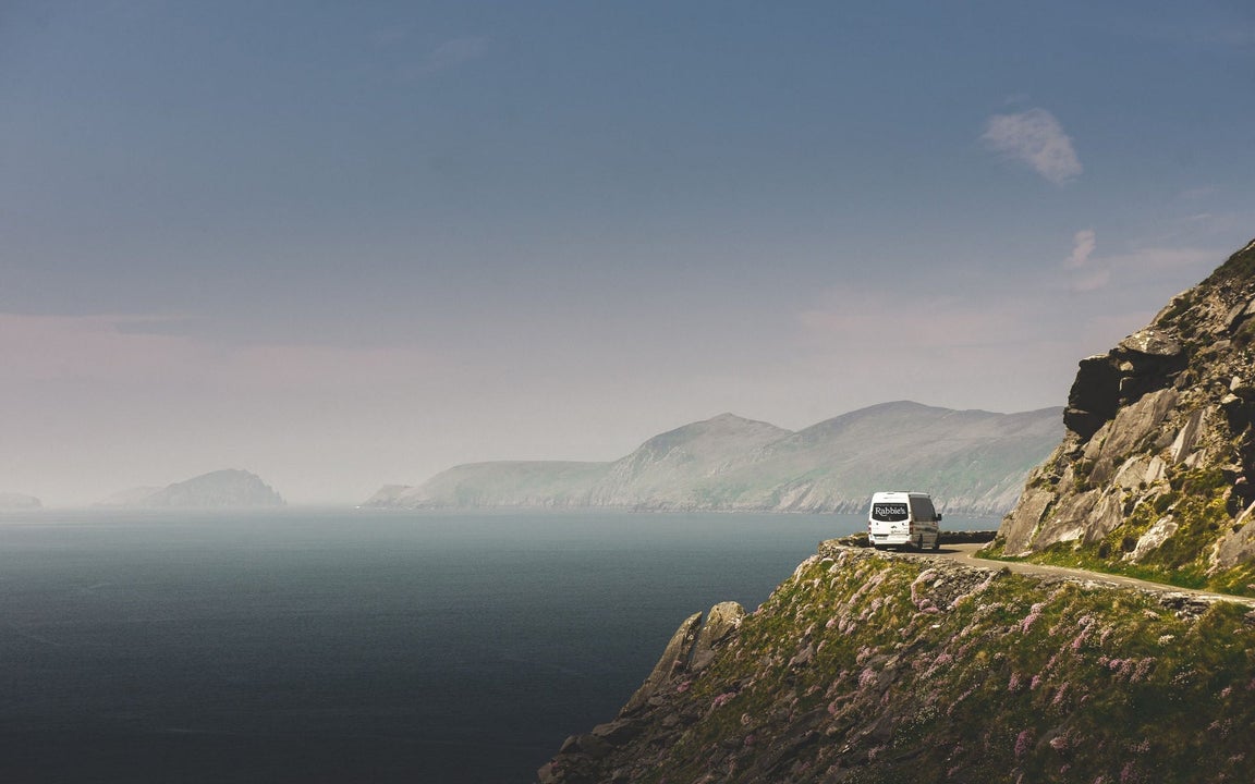 A Rabbies white mini bus driving along a cliff road beside the sea