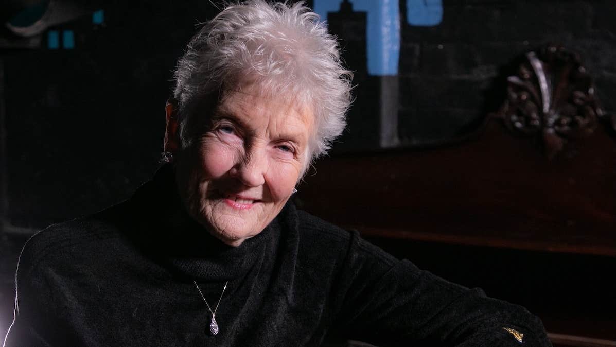 A smiling elderly woman in dark jumper