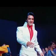 EPiC - Elvis Presley in Concert, slightly blurry photo of smiling man in white suit on black background.