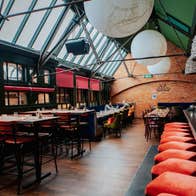 Bar area with exposed brick walls skylights red seating and large pendant lights above the tables