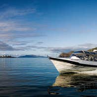 White boat sailing on calm water with cliffs and a lighthouse in the background