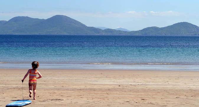 Child on Ballinskelligs Beach pulling surf board 