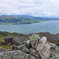 View from above a body of water taken from behind big stones with green fields in the distance