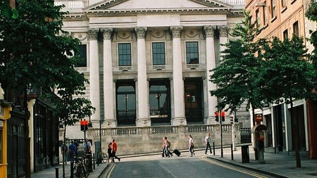 A street view of Dublin City Hall framed by city buildings and trees