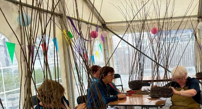 People seated at tables weaving baskets with tail willow canes