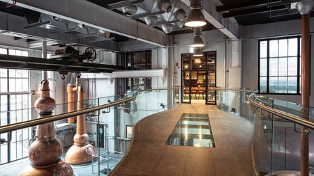 An elevated walk way with an aerial view of copper stills in a distillery