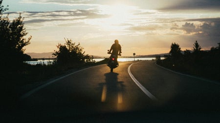 A lone motorbike and rider on a road at sunset