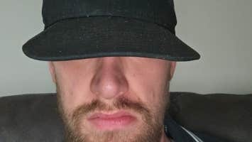 A bearded man with eyes covered by black cap.