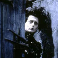 Edward Scissorhands is holding open a door. His has a sad expression.