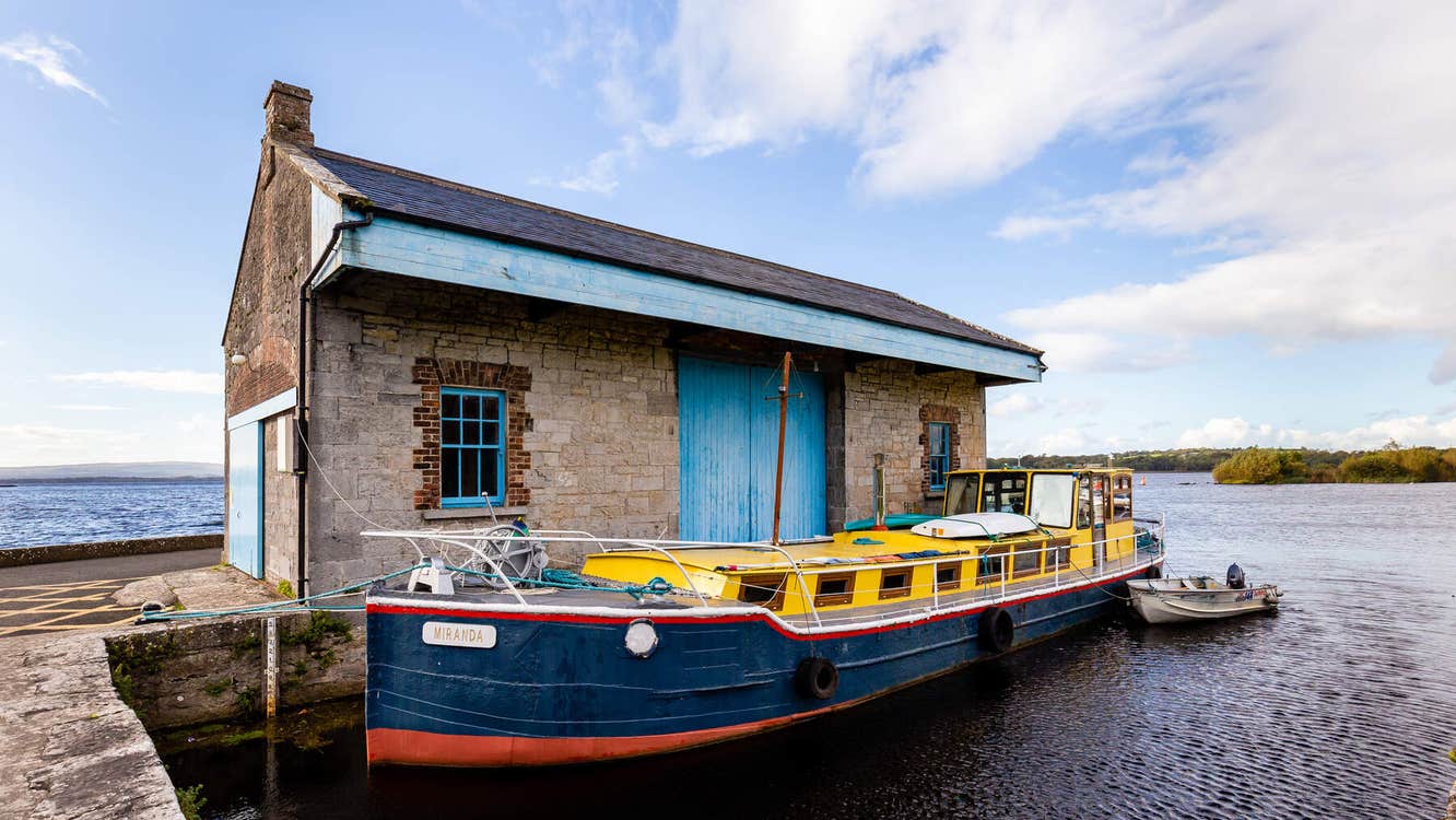 Yellow and navy boat moored outside a boat house with a blue door