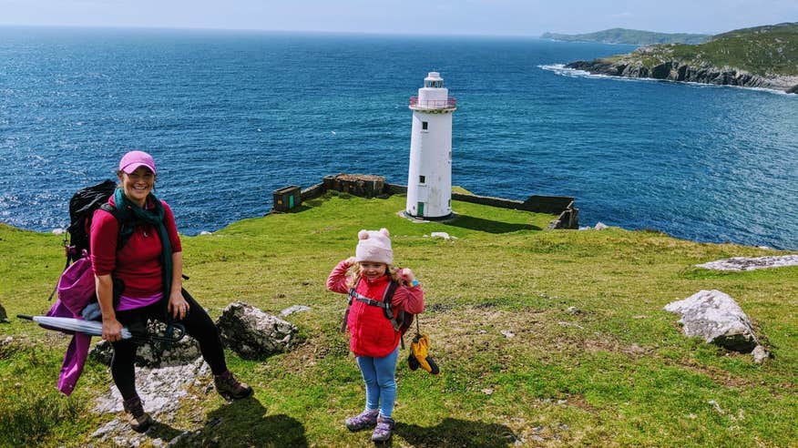 A woman and a child standing on an island with a lighthouse in the background