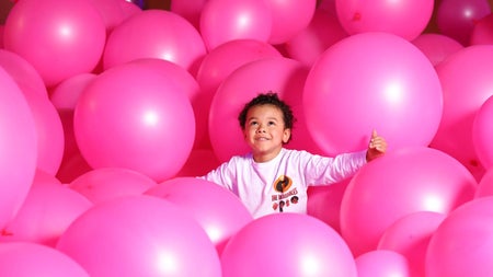 Child looking up while playing among lots of large pink balloons