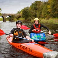 Two people in orange boats kayaking down a river.