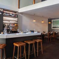 Interior of a bar setting with bar stools at the counter and tables set for service