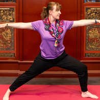 A woman with arms outstretched in a yoga pose with ornate dark red and gold cabinet behind her.