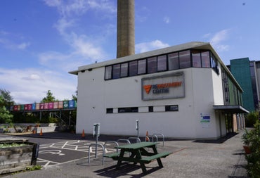 White building with windows on a concrete site with a green picnic bench in front