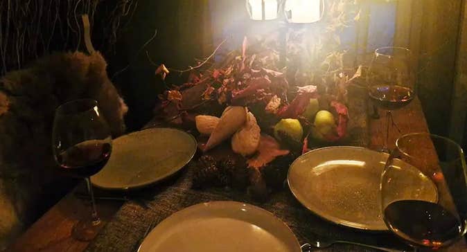 Dark table top lit by candles with empty plates and red wine glasses