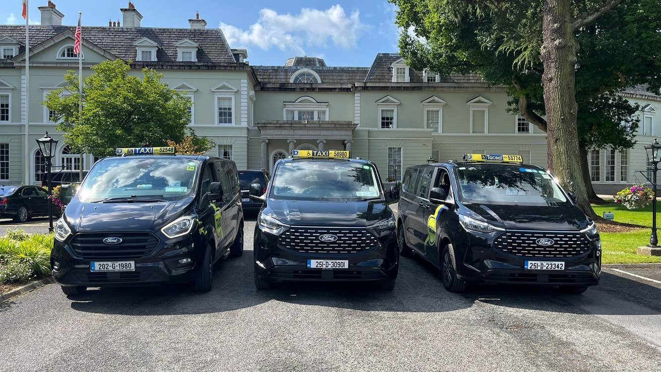 Three black people carriers lined up in front of a historical building