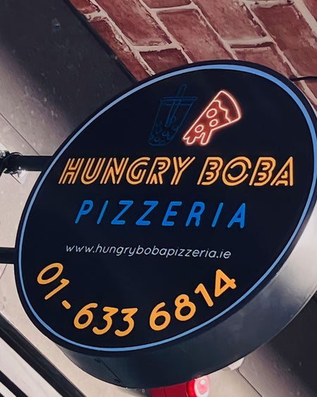 Circular sign for Hungry Boba Pizzeria with telephone number and website on display