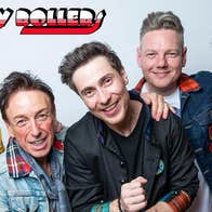 A group of smiling men of various ages, some wearing checked red and black tartan.