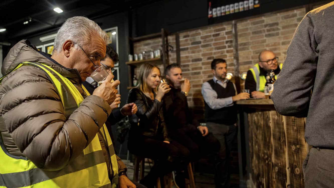 A group of people drinking from a small glass on a brewery tour.