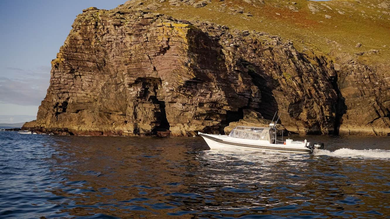 White boat in the sea cruising past a rocky cliff face