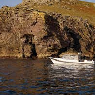 White boat in the sea cruising past a rocky cliff face