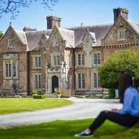 A person sitting under a tree looking at a stately house
