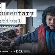 an anxious looking boy in dirty coat holding the wheel of a small boat
