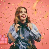 Sadhbh McLoughlin stands in front of a pink background with gold confetti falling around her.