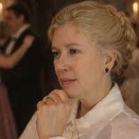 A thoughtful looking woman in white blouse with couples dancing in background lit by candles.