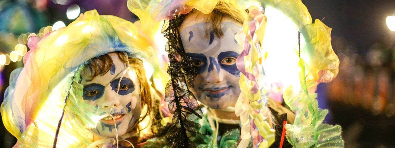 2 young people with faces painted white and dark blue with yellow large headcoverings and costumes.