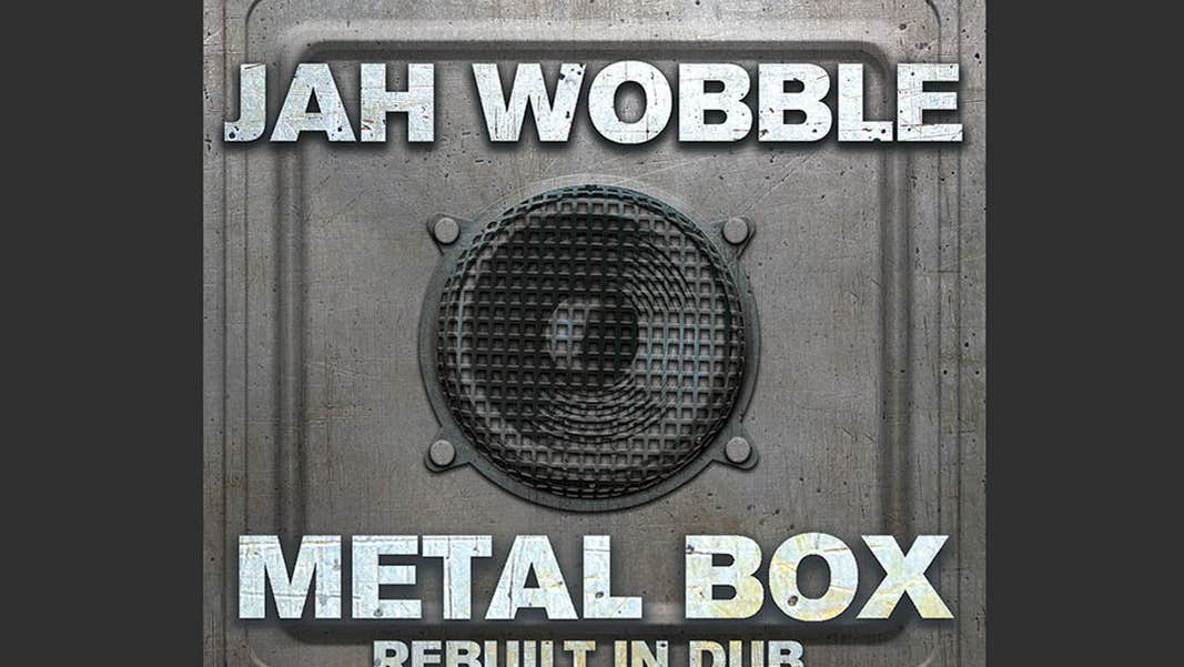 Image of metal grey square box with black speaker in the middle.