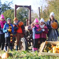 Family enjoying pumpkin patch fun at Wells House & Gardens, choosing pumpkins beside a vintage tractor during the Halloween experience