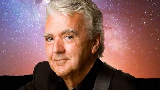 A smiling man against dark blue, purple and orange starry sky