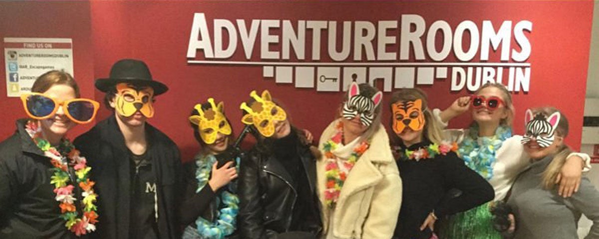 A group of people with animal masks and coloured sunglasses smiling into the camera standing under the Adventure Rooms logo