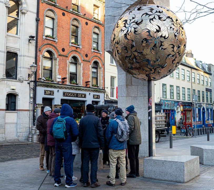 Group of people standing in a circle on a street listening to a guide with a gold globe above them